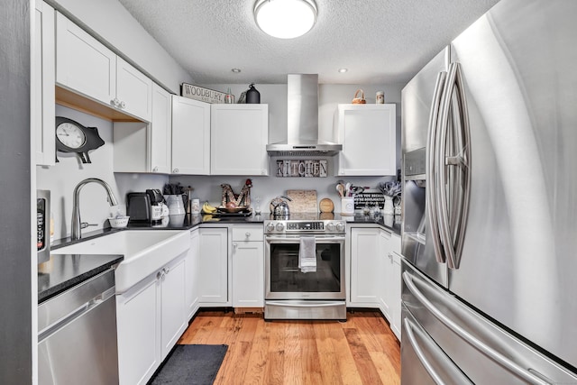 kitchen featuring light wood finished floors, a sink, stainless steel appliances, dark countertops, and wall chimney exhaust hood