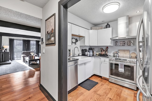 kitchen featuring a sink, white cabinetry, stainless steel appliances, wall chimney exhaust hood, and light wood finished floors