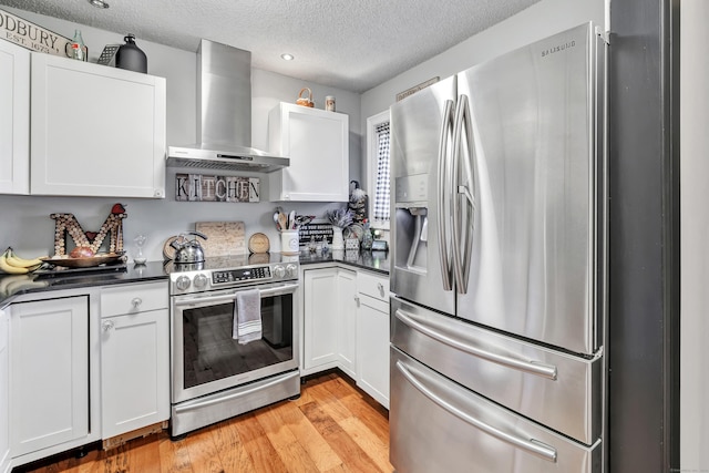 kitchen featuring dark countertops, stainless steel appliances, light wood-type flooring, and wall chimney range hood