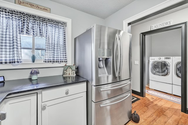 kitchen featuring washing machine and dryer, light wood-style flooring, stainless steel fridge, a textured ceiling, and white cabinetry