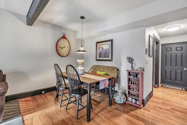 dining area featuring beam ceiling, a textured ceiling, baseboards, and hardwood / wood-style floors