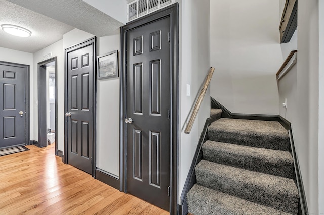 entryway featuring stairway, baseboards, visible vents, light wood finished floors, and a textured ceiling