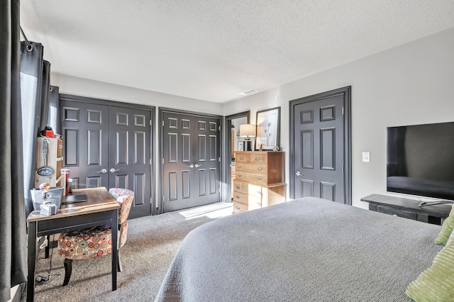 bedroom featuring visible vents, a textured ceiling, carpet, and multiple closets