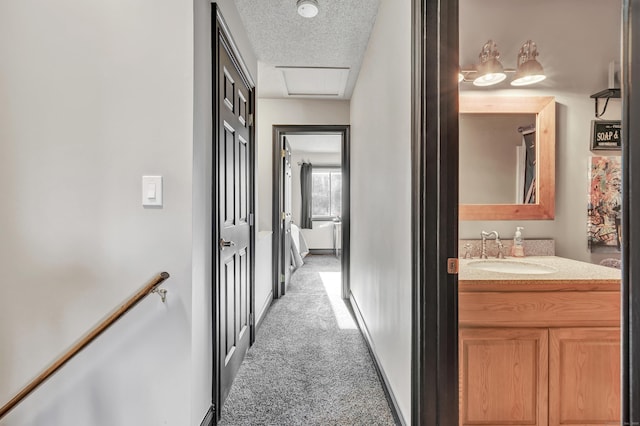 corridor with a sink, a textured ceiling, baseboards, light colored carpet, and attic access