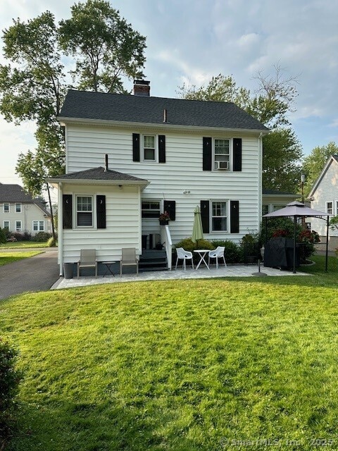 rear view of property with entry steps, a chimney, a yard, and a patio