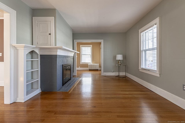 unfurnished living room with baseboards, radiator, a brick fireplace, and hardwood / wood-style floors