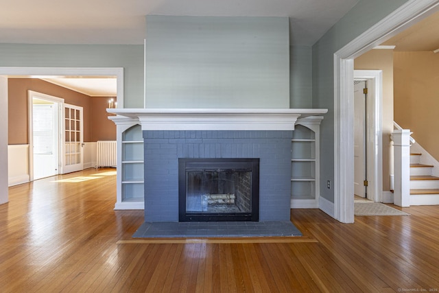 unfurnished living room featuring radiator, a brick fireplace, hardwood / wood-style floors, and stairs