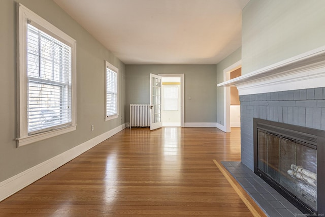 unfurnished living room featuring a brick fireplace, radiator, wood finished floors, and baseboards