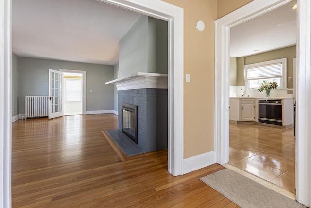 unfurnished living room featuring wood finished floors, baseboards, radiator heating unit, a fireplace, and a sink