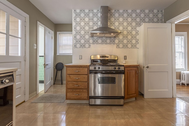 kitchen featuring light countertops, wall chimney range hood, radiator, and stainless steel gas range