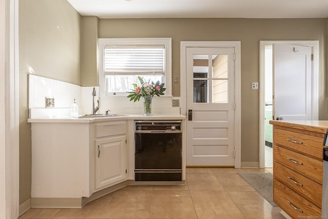 kitchen with dishwasher, light countertops, light tile patterned flooring, white cabinetry, and a sink