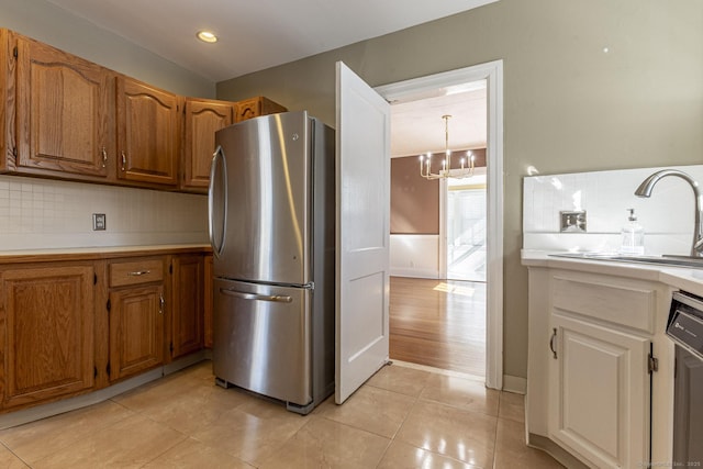 kitchen featuring light tile patterned floors, freestanding refrigerator, light countertops, dishwasher, and backsplash