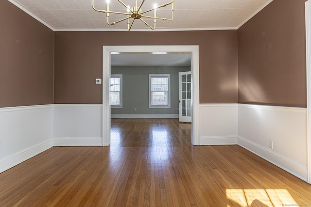 spare room with hardwood / wood-style floors, an inviting chandelier, crown molding, and baseboards