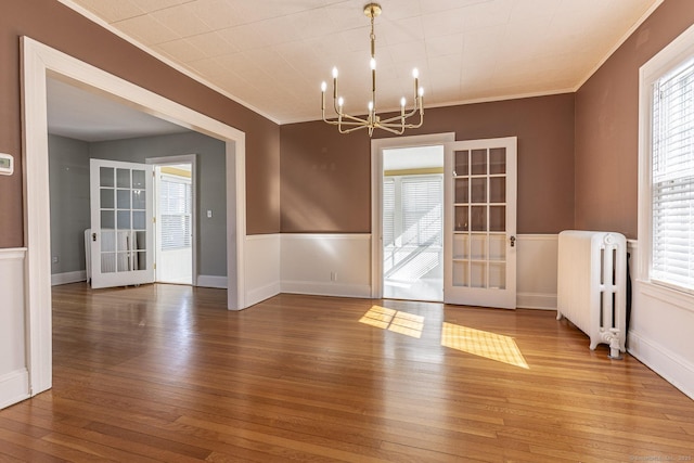 unfurnished dining area with radiator, plenty of natural light, hardwood / wood-style flooring, crown molding, and a chandelier