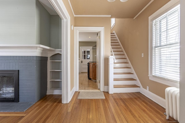 stairs with hardwood / wood-style floors, radiator, a fireplace, crown molding, and baseboards