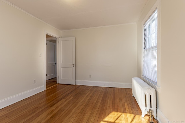 unfurnished room featuring baseboards, wood-type flooring, radiator, and crown molding