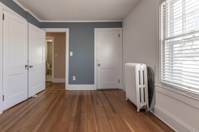 unfurnished bedroom with hardwood / wood-style floors, multiple windows, radiator, and ornamental molding