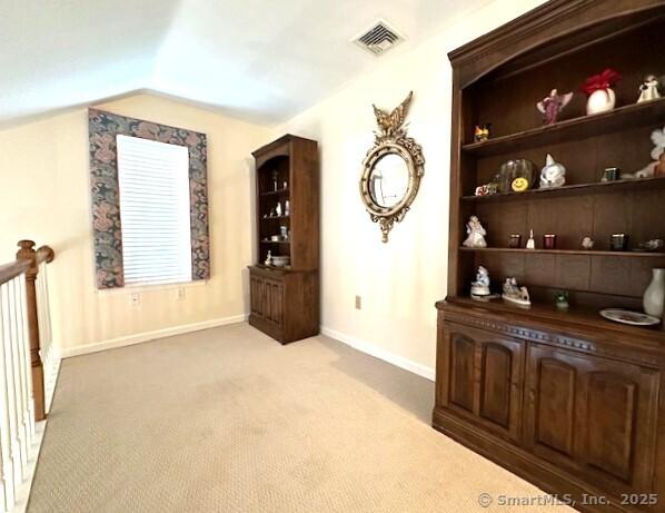 interior space featuring visible vents, baseboards, built in features, vaulted ceiling, and light carpet