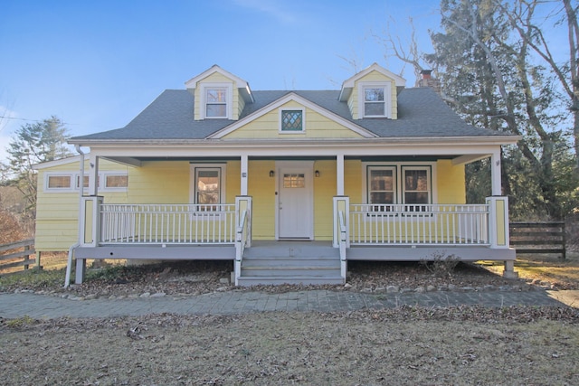 view of front of property featuring a porch, a shingled roof, a chimney, and fence