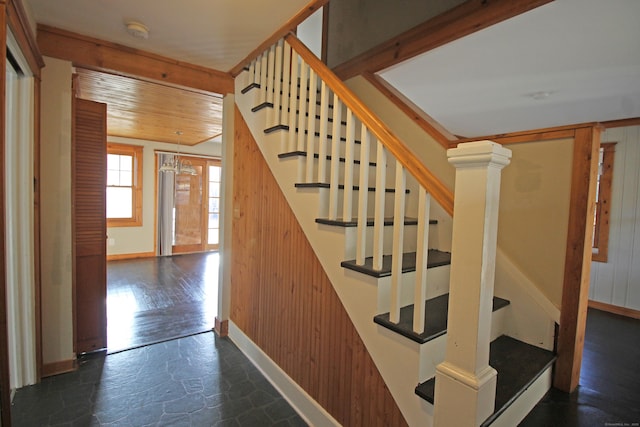 stairs featuring a notable chandelier, stone tile flooring, wooden ceiling, wood walls, and baseboards