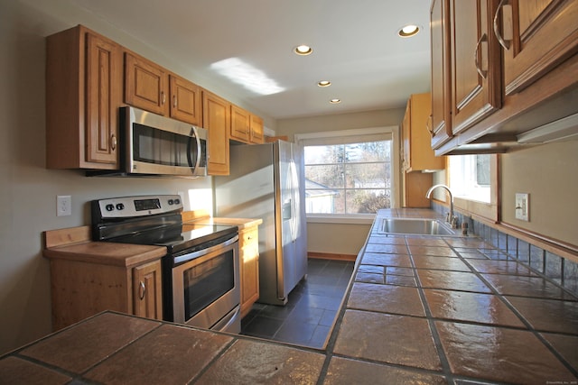 kitchen with brown cabinetry, recessed lighting, a sink, stainless steel appliances, and tile counters