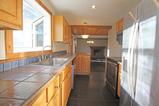 kitchen with tile countertops, a peninsula, dark tile patterned flooring, a sink, and appliances with stainless steel finishes