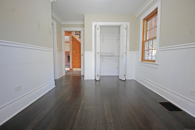 empty room with visible vents, crown molding, dark wood-type flooring, and a wainscoted wall