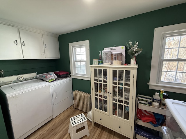 clothes washing area featuring washer and dryer, cabinet space, radiator heating unit, and light wood finished floors