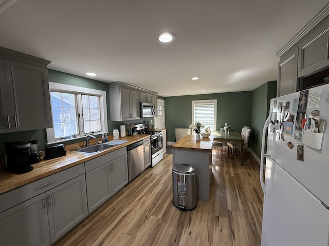 kitchen with wood finished floors, gray cabinets, a sink, butcher block countertops, and stainless steel appliances