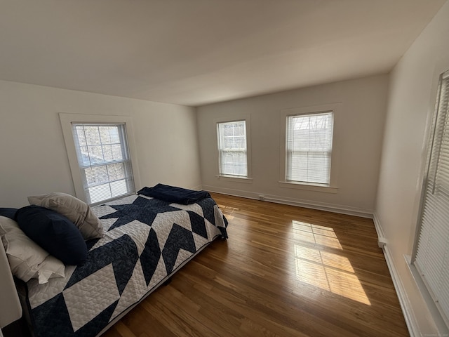 bedroom with multiple windows, wood finished floors, and baseboards