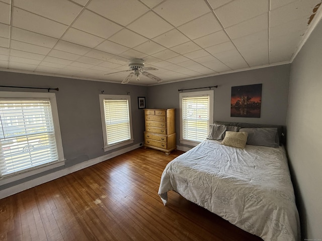 bedroom featuring ornamental molding, a drop ceiling, wood-type flooring, baseboards, and ceiling fan