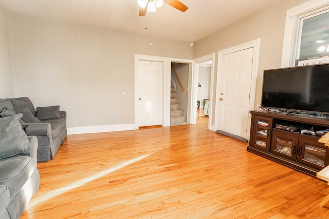 living room with light wood finished floors, baseboards, stairs, and a ceiling fan