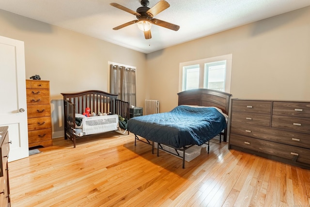 bedroom with a ceiling fan, radiator heating unit, and light wood finished floors