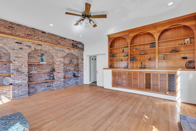 unfurnished living room with a ceiling fan, recessed lighting, wood finished floors, and brick wall