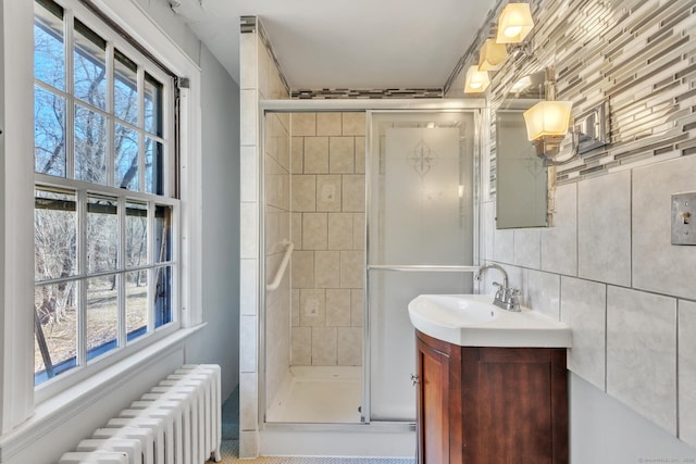 bathroom featuring a stall shower, tasteful backsplash, radiator heating unit, tile walls, and vanity