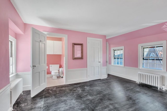 unfurnished bedroom with a wainscoted wall, dark wood-style floors, ensuite bath, and radiator heating unit