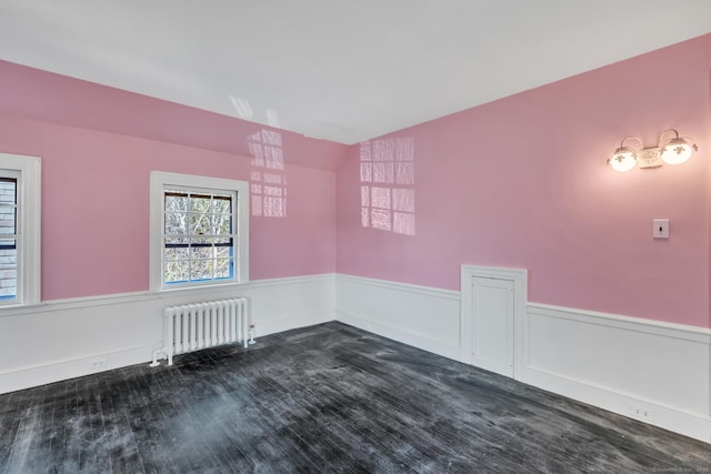 spare room with dark wood-style floors, wainscoting, radiator, and lofted ceiling