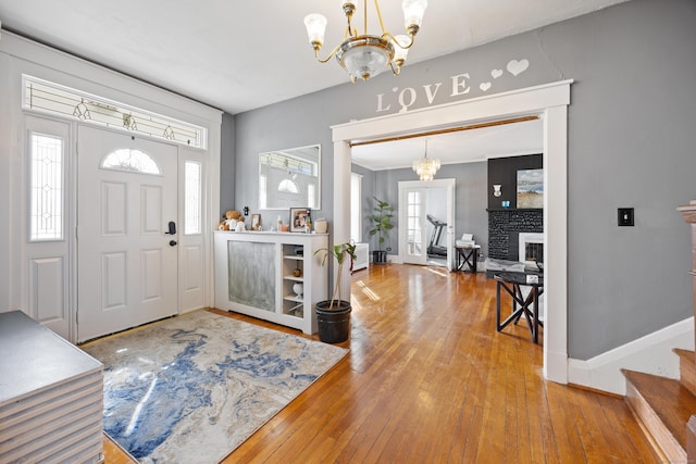 entrance foyer with a fireplace with raised hearth, baseboards, an inviting chandelier, and hardwood / wood-style floors