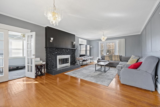 living room featuring hardwood / wood-style floors, ornamental molding, french doors, a glass covered fireplace, and a chandelier