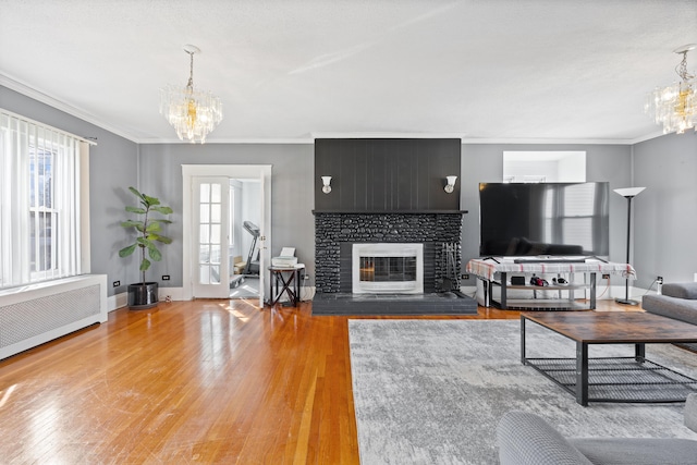 living room featuring light wood finished floors, radiator heating unit, ornamental molding, an inviting chandelier, and a glass covered fireplace