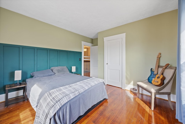 bedroom featuring a decorative wall, wainscoting, and wood-type flooring