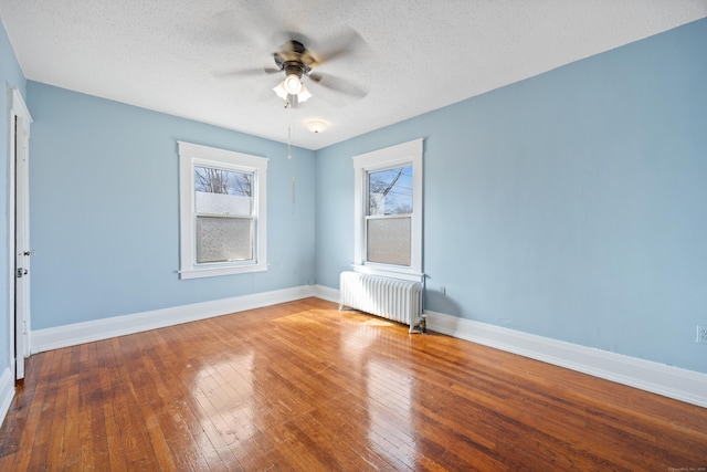 empty room featuring radiator, baseboards, wood-type flooring, and a textured ceiling