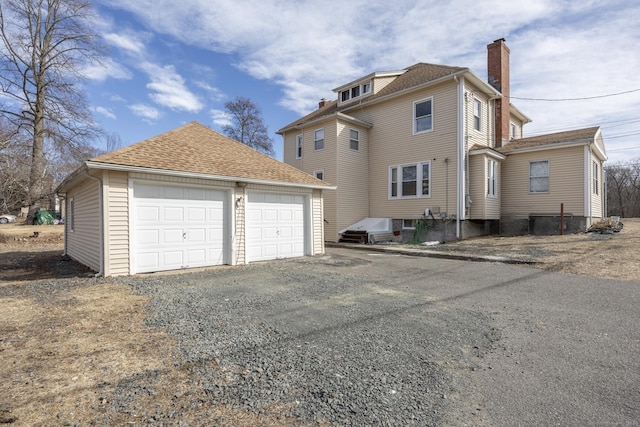 exterior space with a detached garage, roof with shingles, an outdoor structure, and a chimney