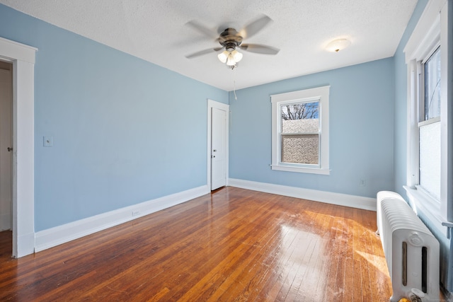 empty room with baseboards, wood-type flooring, a textured ceiling, and radiator heating unit