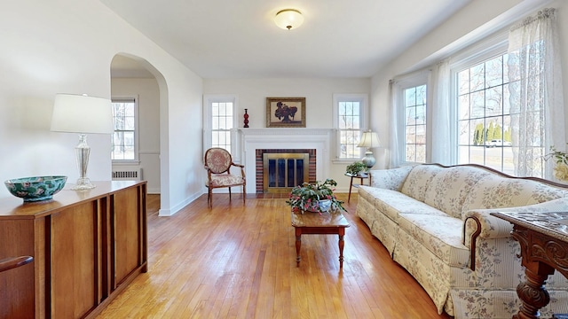 living room featuring light wood-style flooring, radiator heating unit, arched walkways, a fireplace, and baseboards