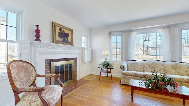 living area featuring a brick fireplace, wood finished floors, baseboards, and a healthy amount of sunlight