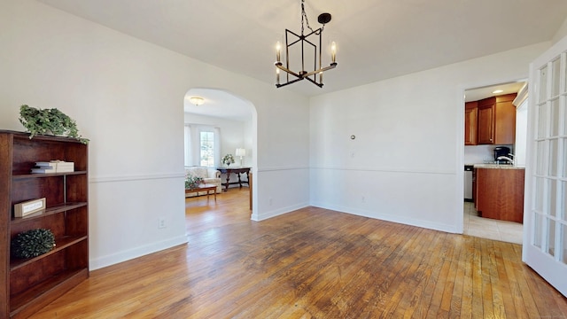 dining room with arched walkways, baseboards, light wood-type flooring, and an inviting chandelier