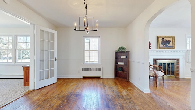 unfurnished dining area with hardwood / wood-style floors, radiator, a fireplace, arched walkways, and a baseboard heating unit