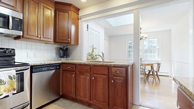 kitchen featuring light stone counters, a sink, stainless steel appliances, a notable chandelier, and tasteful backsplash