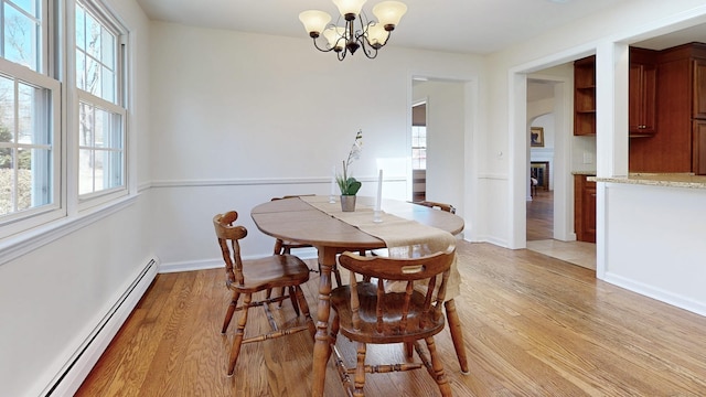 dining space with baseboards, light wood-style flooring, a glass covered fireplace, baseboard heating, and a chandelier